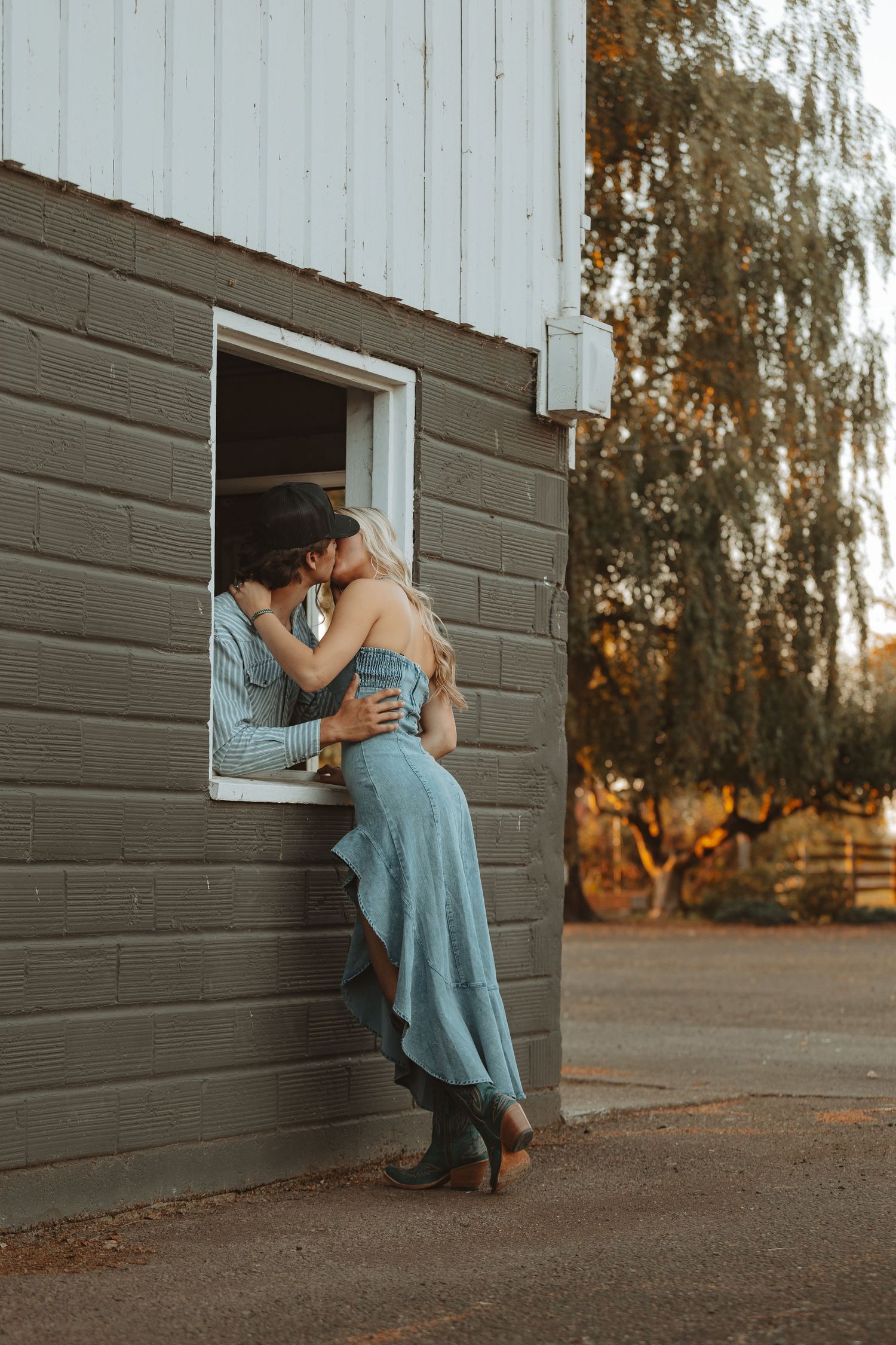 Couple sharing a tender kiss through an open barn window at warm sunset on a farm.