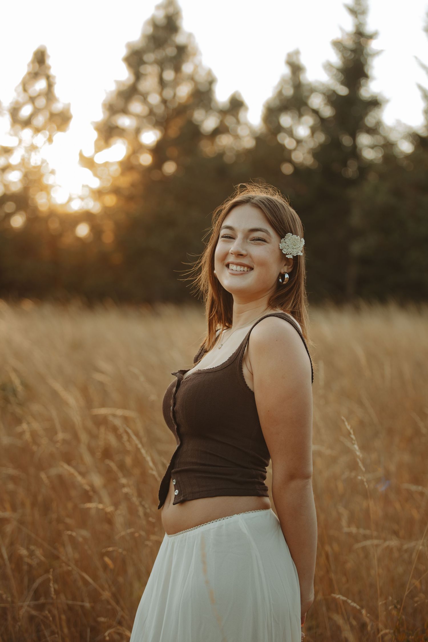 Joyful sunset portrait in a field with warm golden light filtering through pine trees in the background.