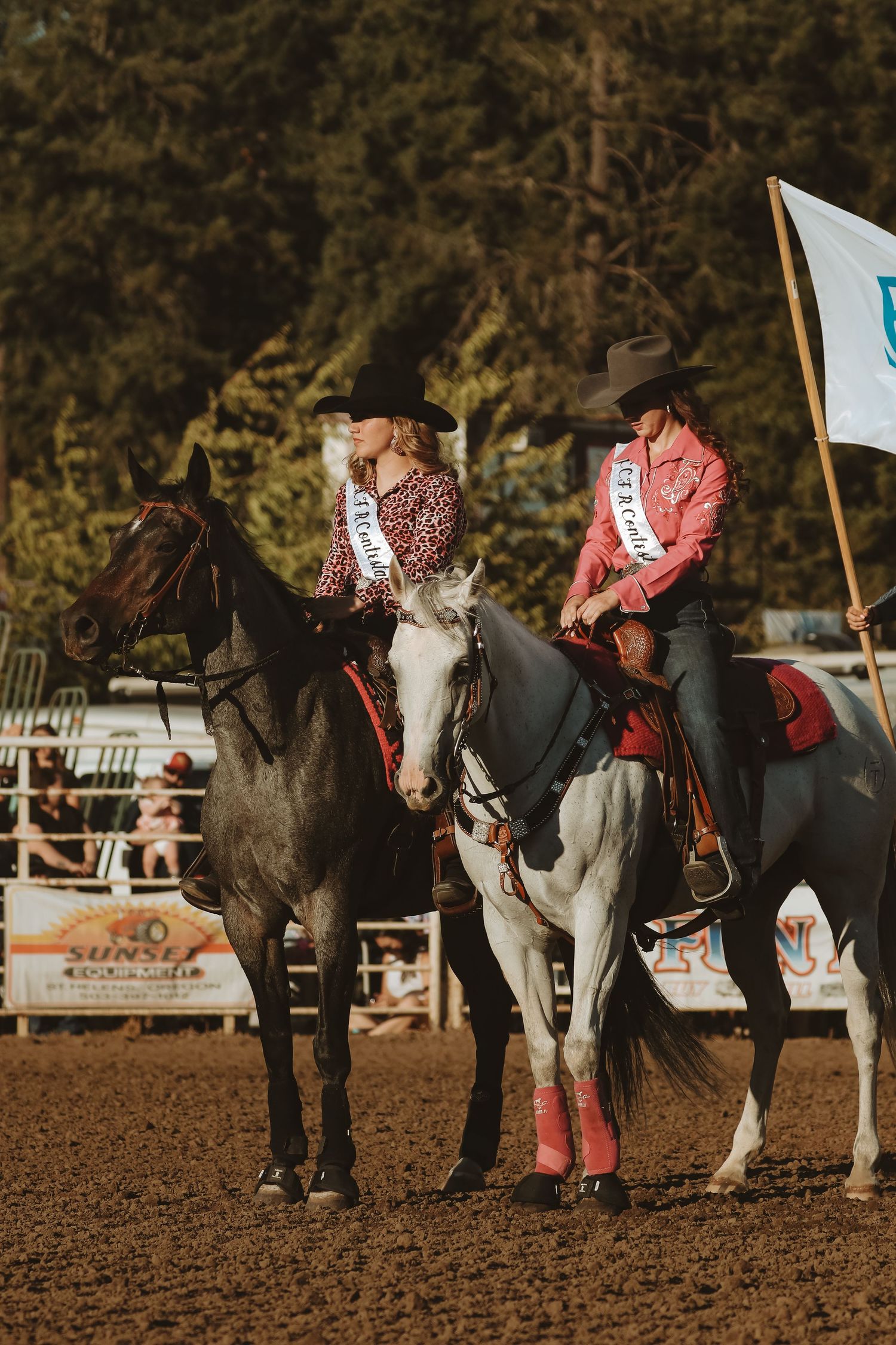 Two riders in western attire sit atop their horses during a rodeo competition.