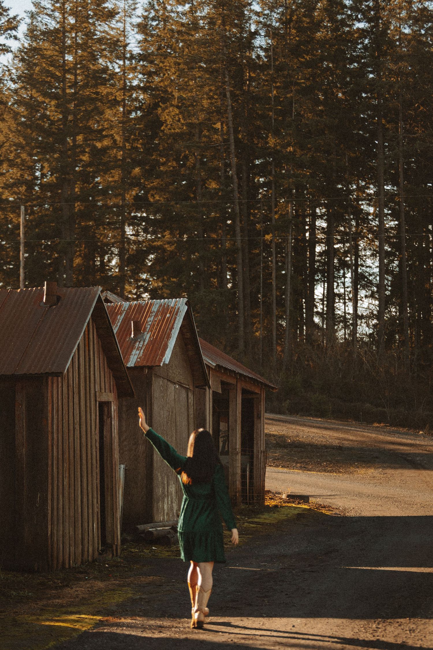 Figure in green clothing dances joyfully near wooden buildings during sunset.