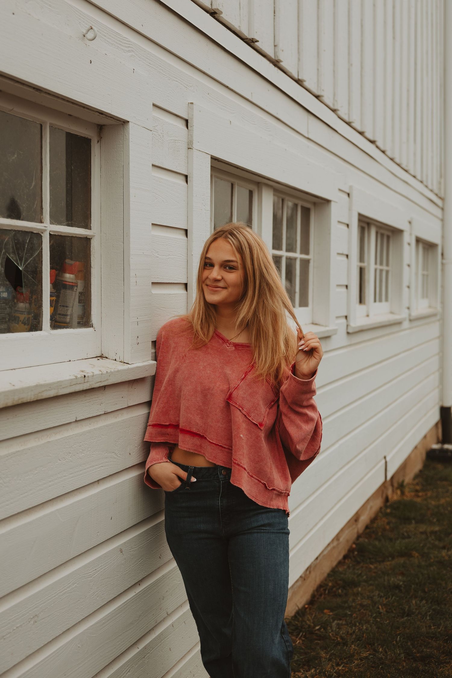 Casual fashion shoot with coral sweater and jeans against white architectural background.