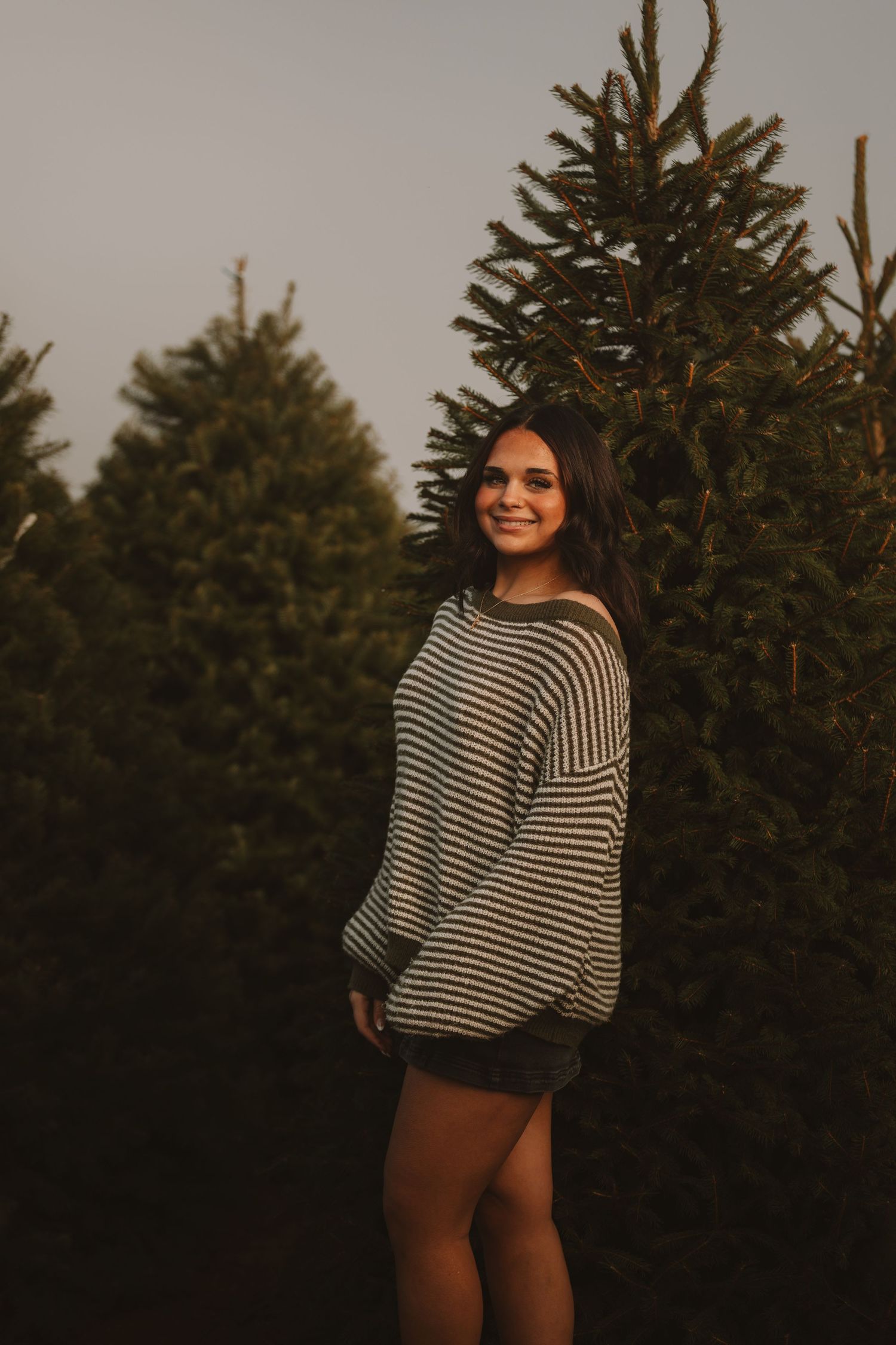 Sunset photoshoot with evergreen trees showing striped sweater fashion poses.