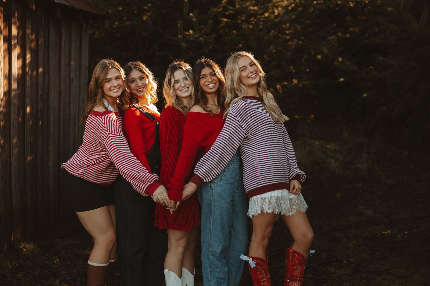 A group of friends in winter outfits pose together in front of a dark wooden wall during golden hour.