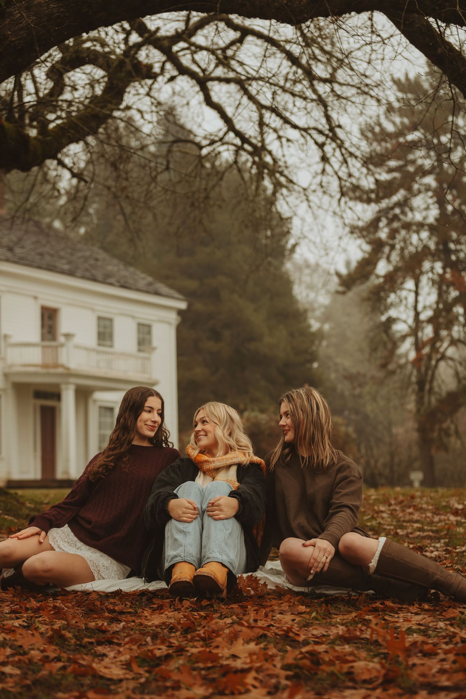 Group lying on fallen autumn leaves in front of a white house on a misty day.