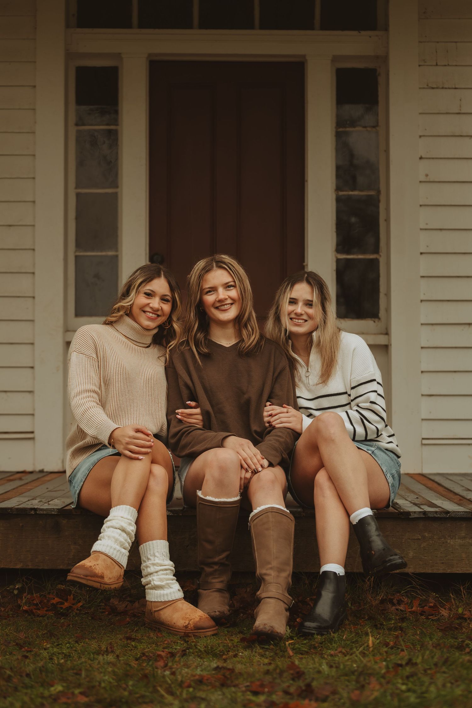 A row of boots and socks shown from the knees down as friends sit together on a porch step.