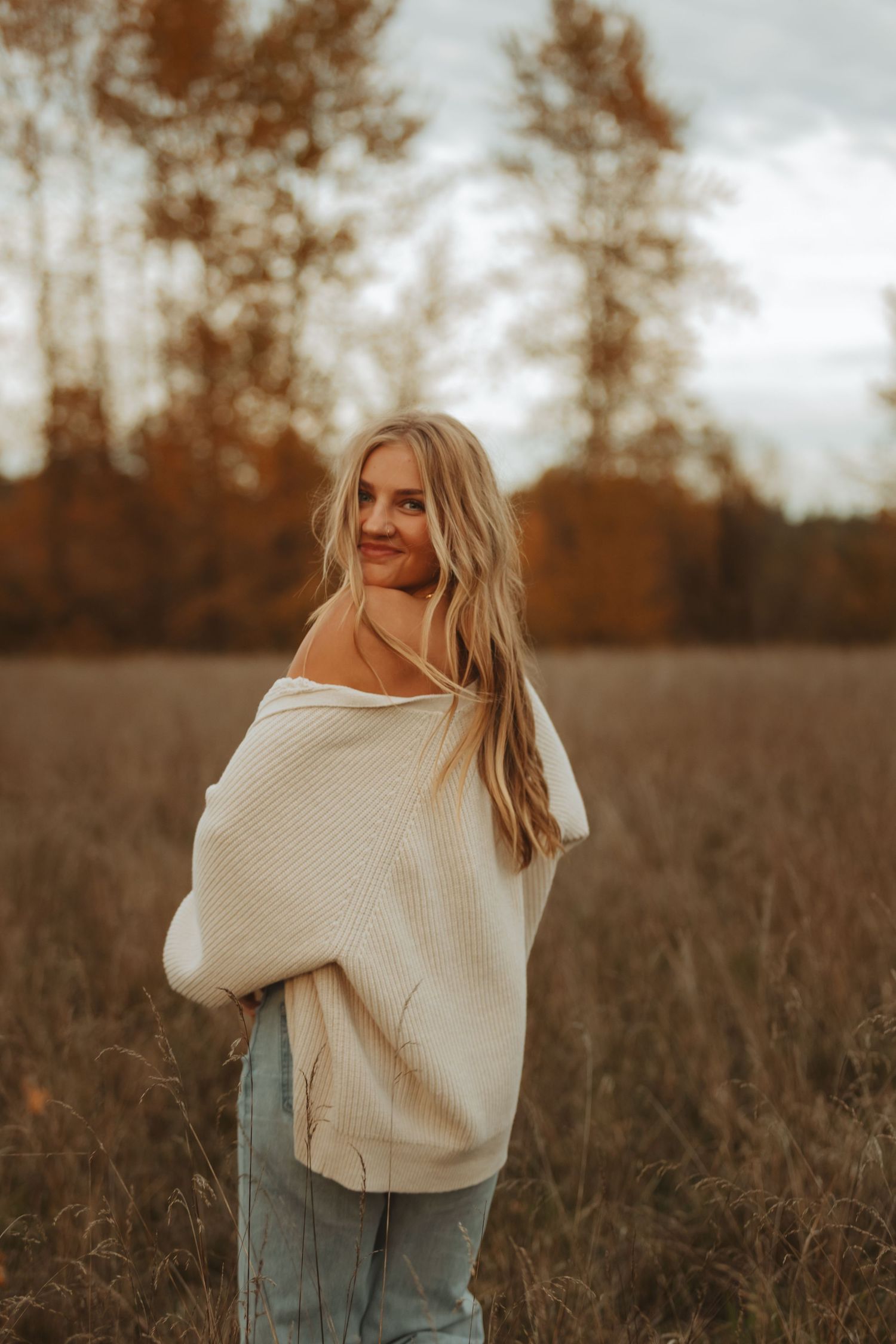 Person wearing a cozy cream sweater poses in a rustic fall field during golden hour.