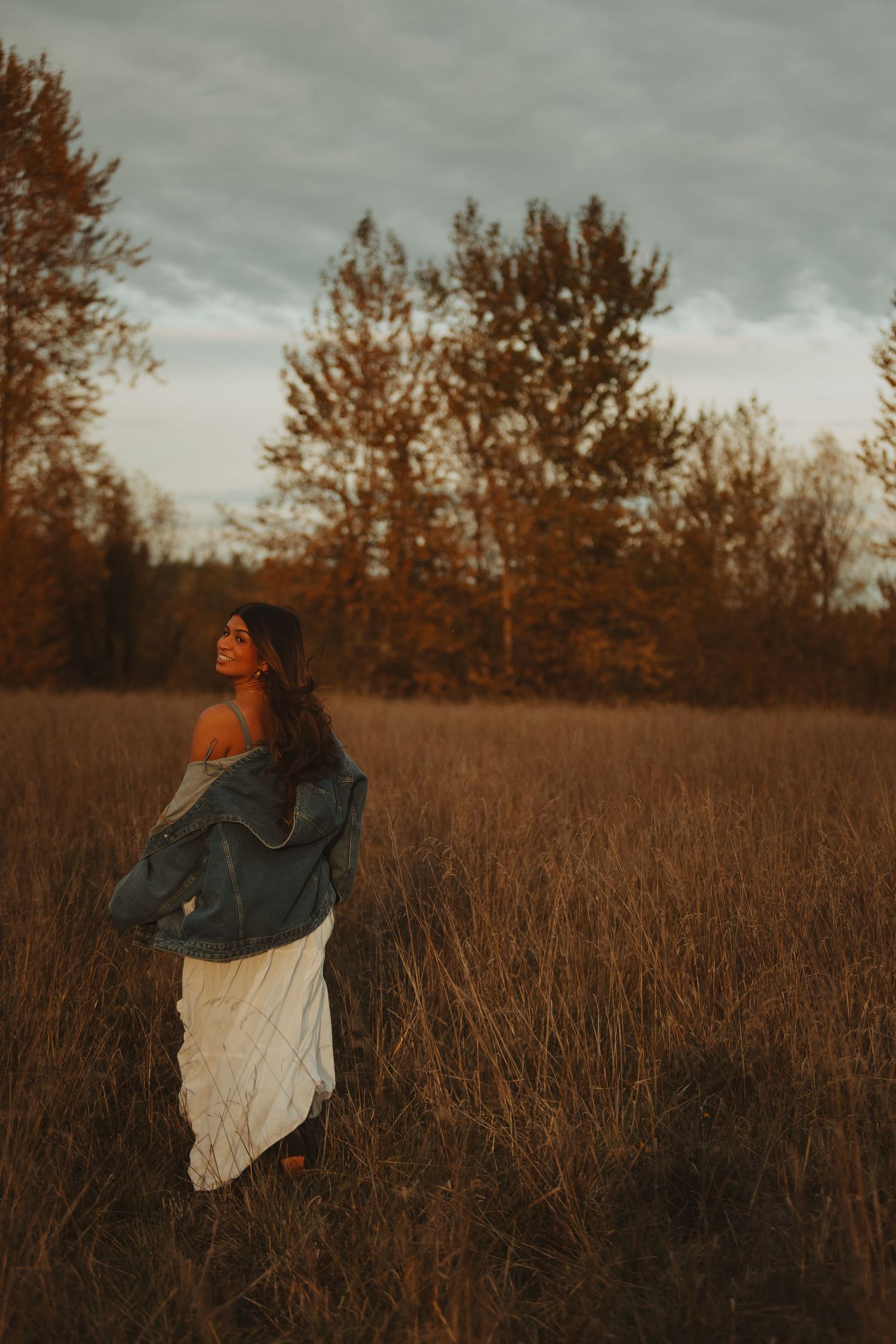 Person twirling in white dress against autumn field at sunset.