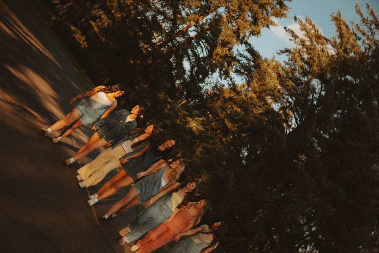 Group of friends standing together outdoors near tall trees during golden hour sunset.