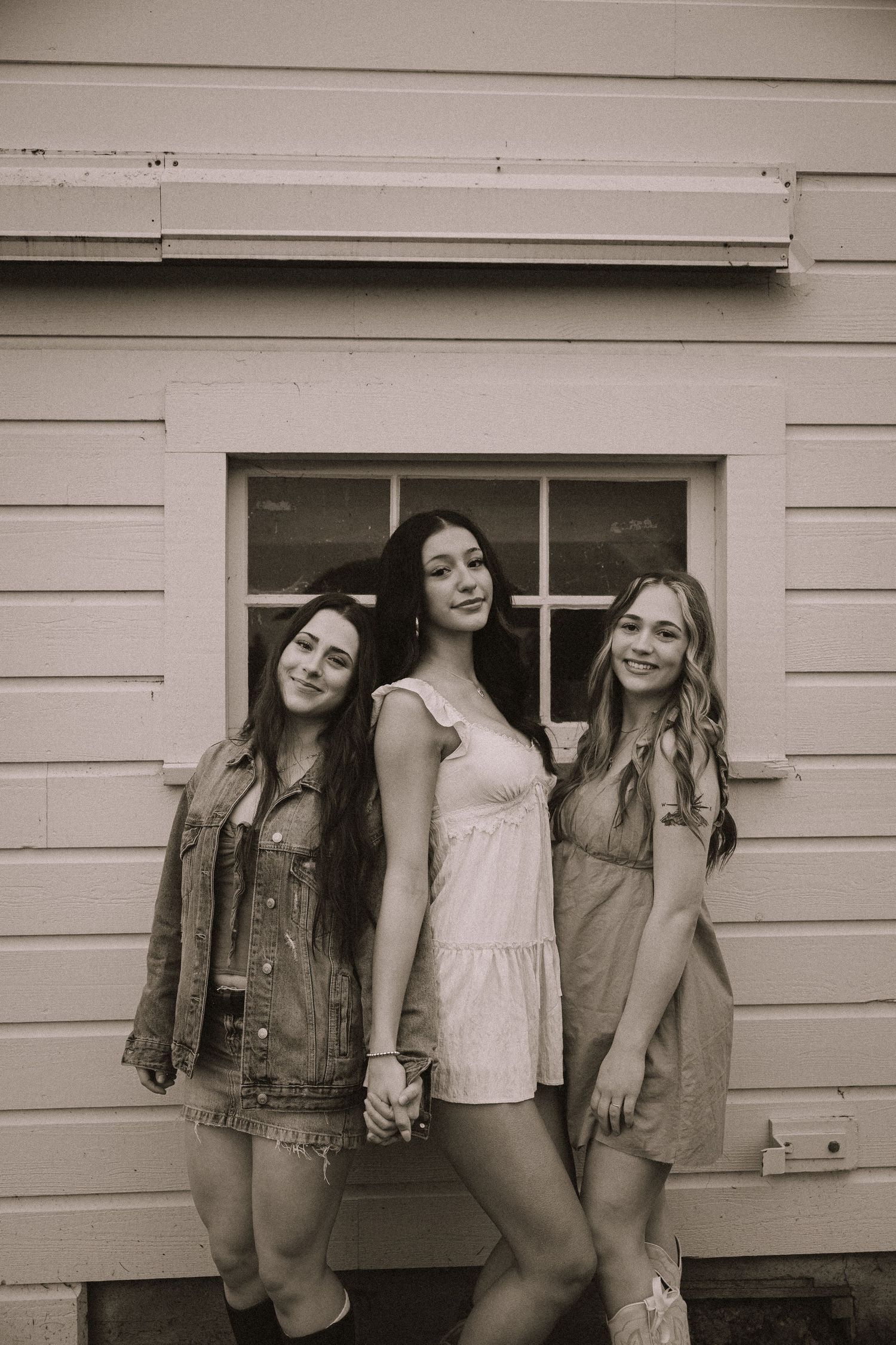 A vintage-style black and white photo of friends posing together against a white building exterior.