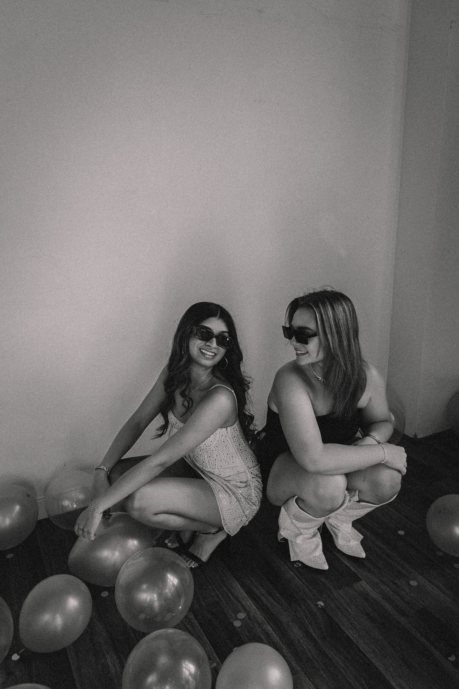 Black and white photo of two people posing with balloons in artistic setting.