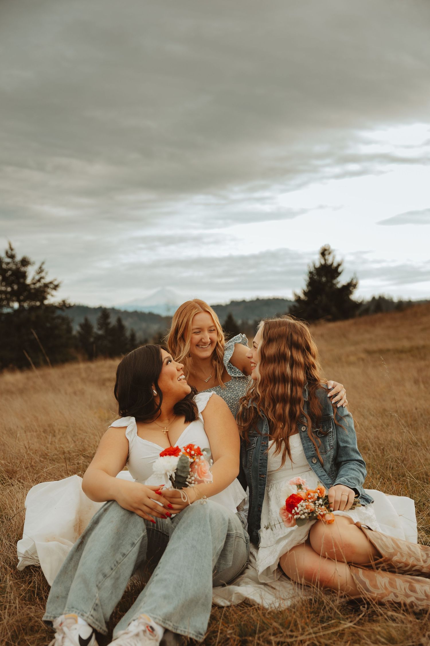 Three friends share intimate laughs while laying in tall grass at sunset.