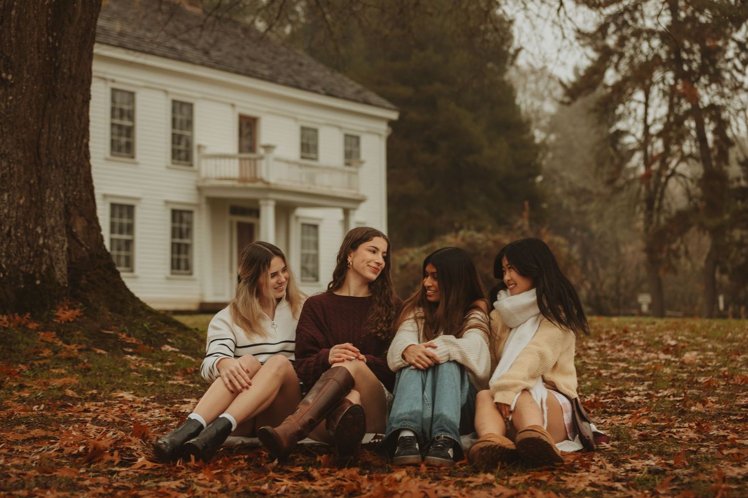 People sitting together on autumn leaves during a moody fall photoshoot outdoors.