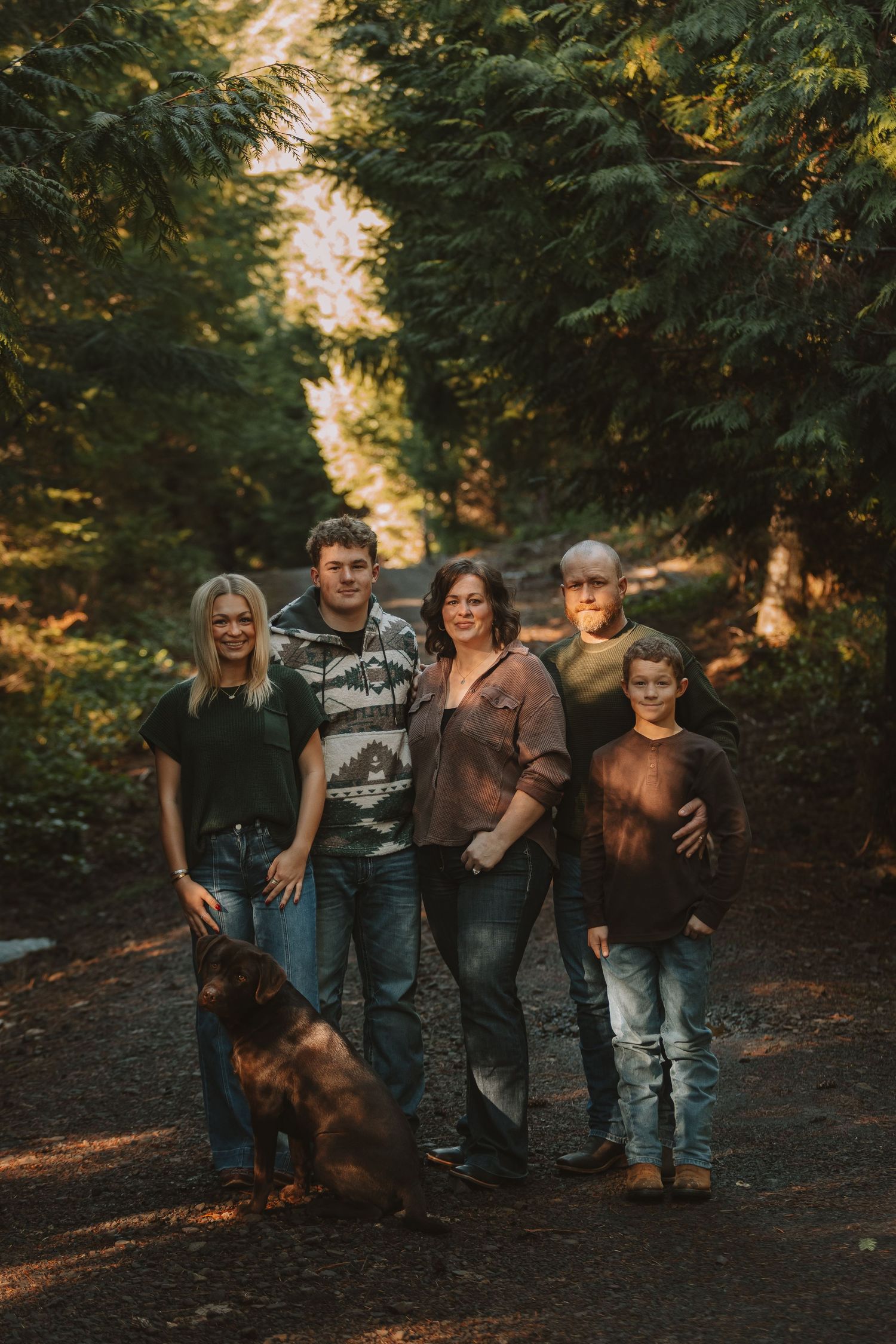 A group poses together on a forest path during golden hour with their dog in an autumn setting.