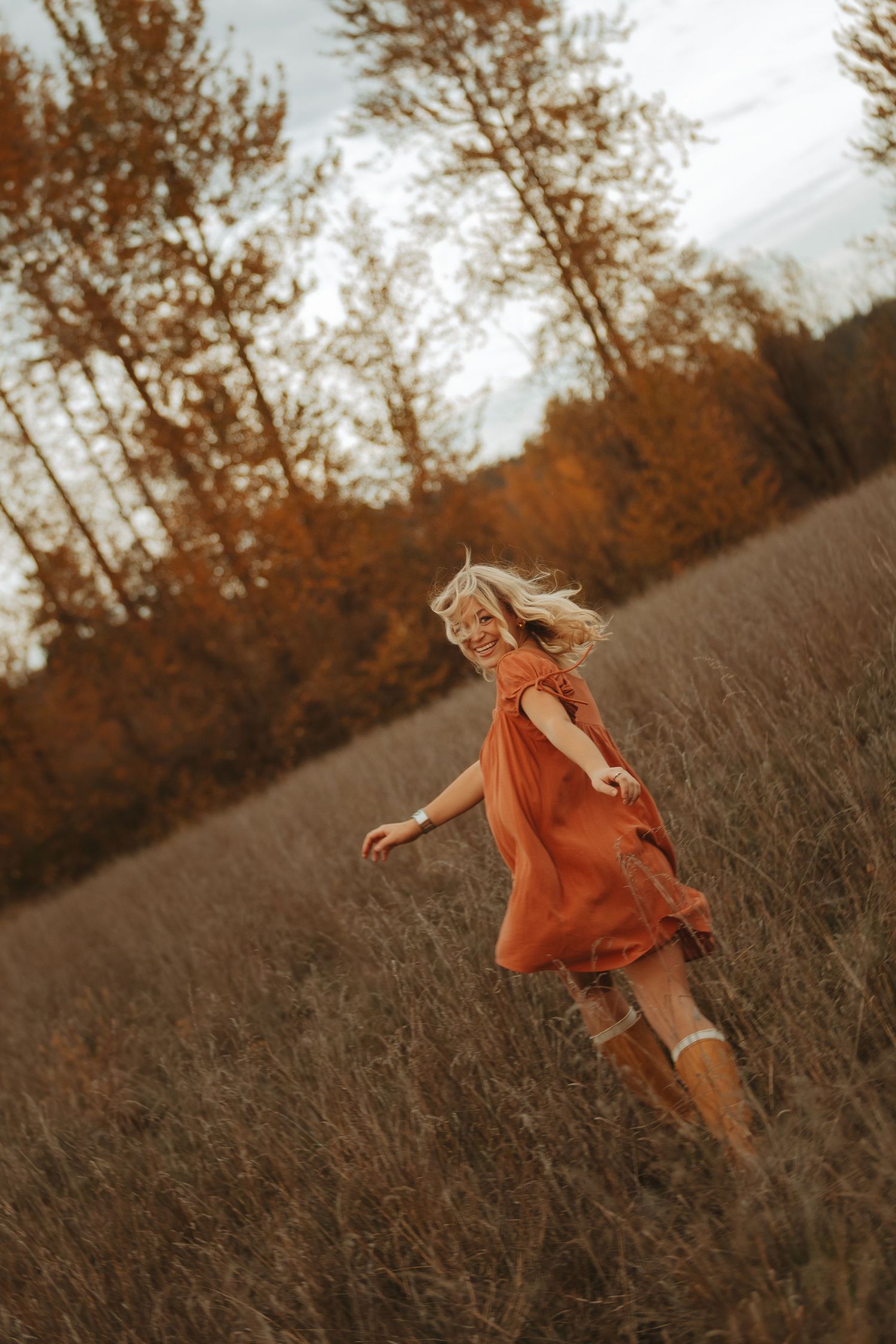 Figure in an orange dress twirls playfully through tall grass during autumn sunset.