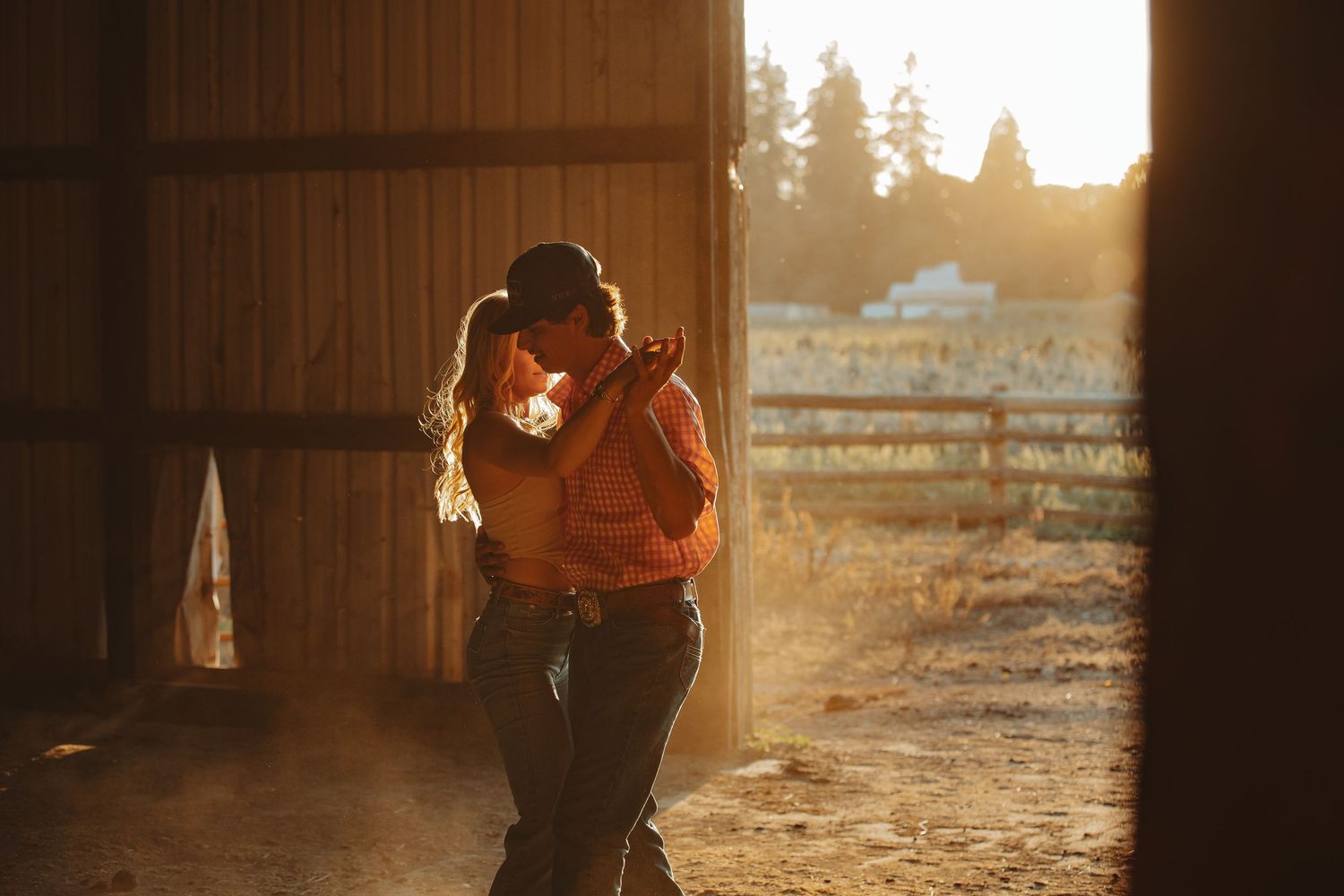Couple embracing and kissing in a warm sunlit barn doorway with golden hour light.