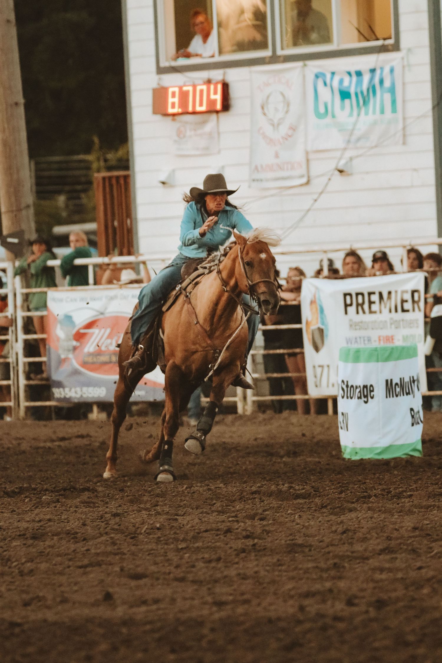 Riders compete in a western rodeo event with advertising banners visible in background.