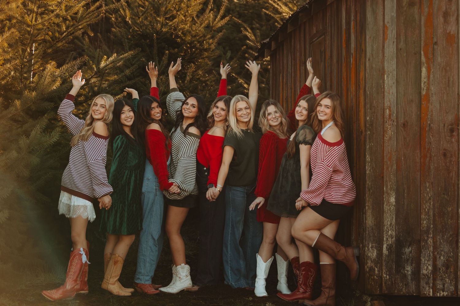 A group of people stand together against a rustic wooden barn wall wearing coordinated casual outfits.