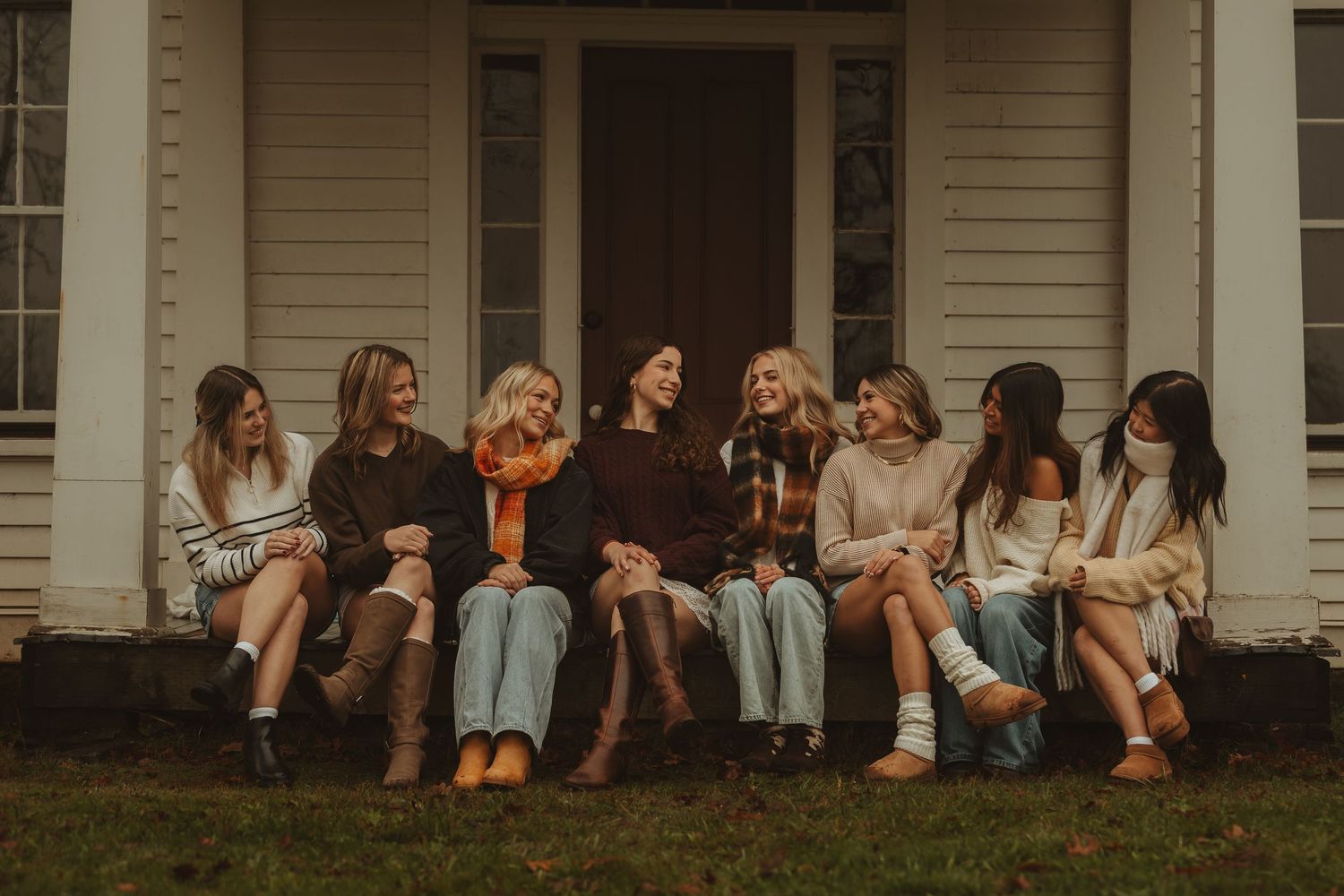 A row of people sitting on a porch ledge in casual clothing during a sunny day.