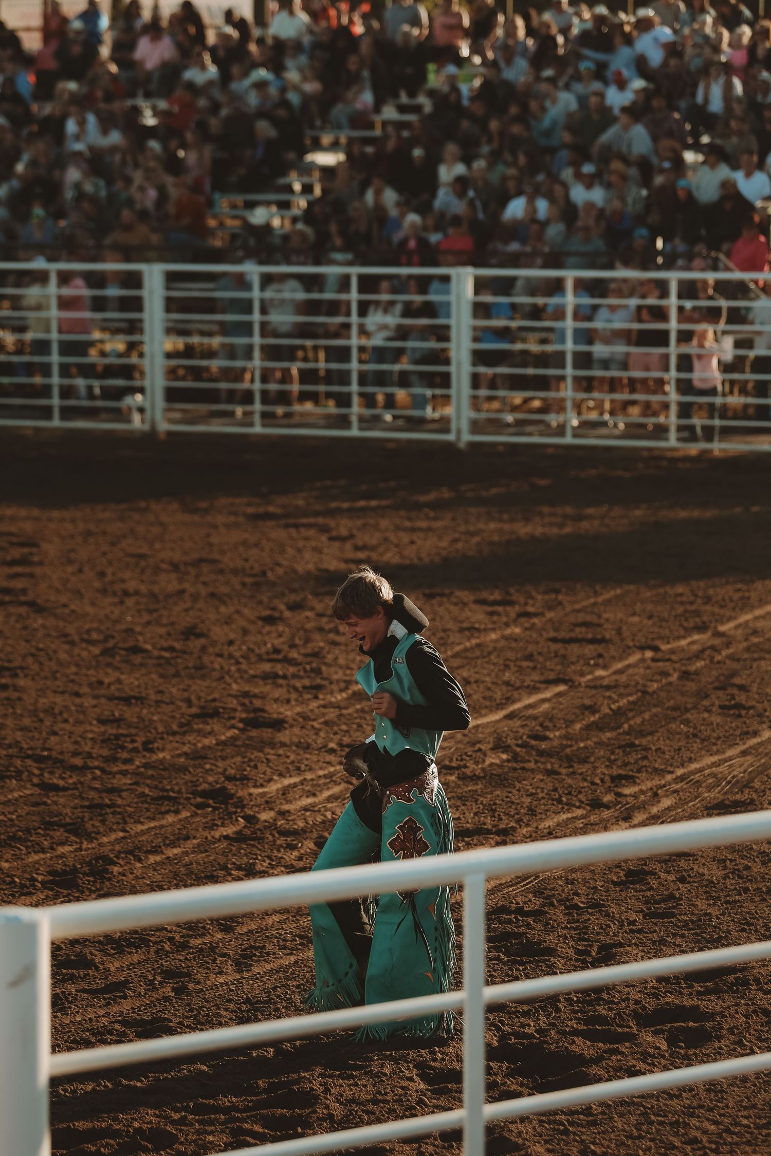 A rodeo performer in green attire leans against white arena fencing during competition.