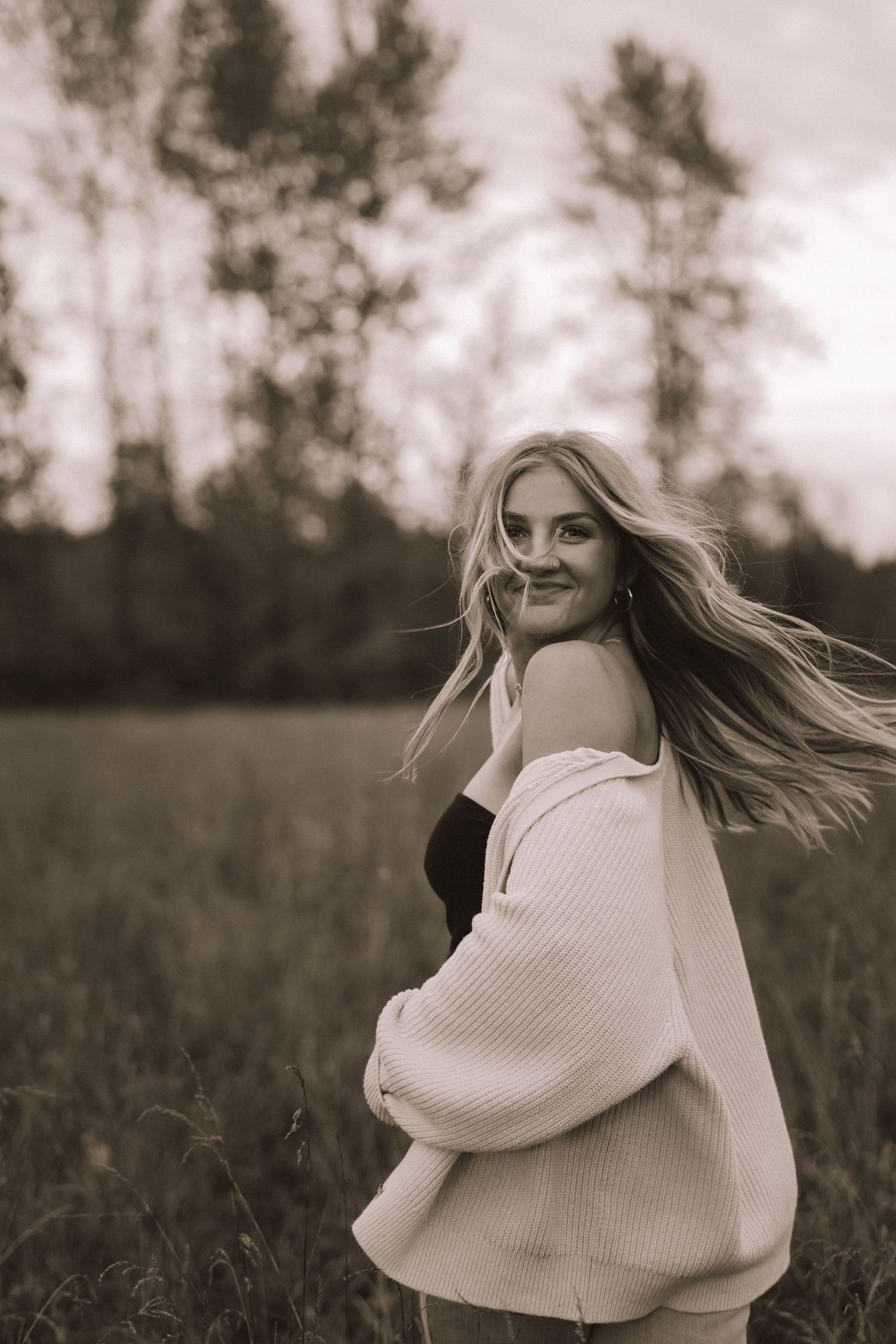 Person in cream sweater spins joyfully in field during black and white photoshoot.