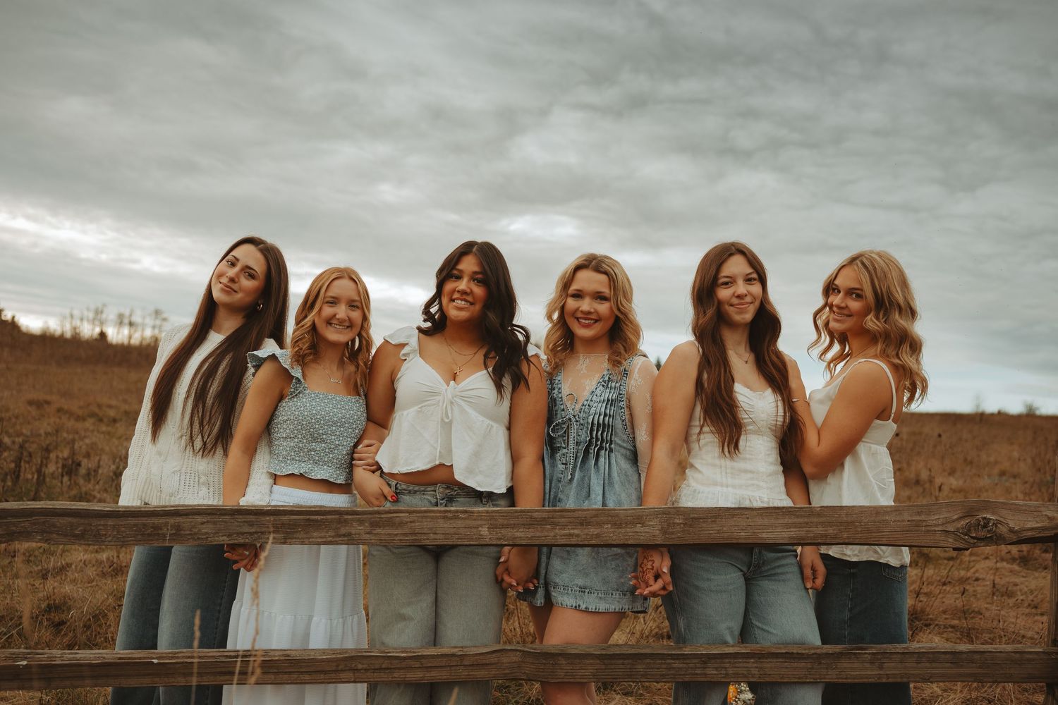 A group of people in coordinated blue and gray outfits pose together on a rustic wooden fence at sunset.