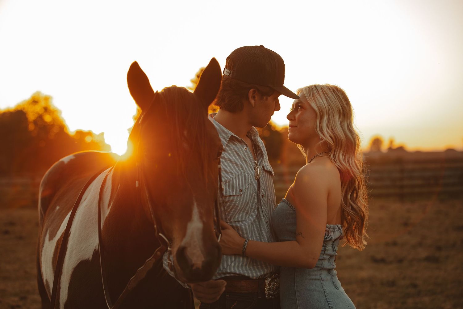 Couple with a paint horse sharing a tender moment during a beautiful golden sunset on a ranch.