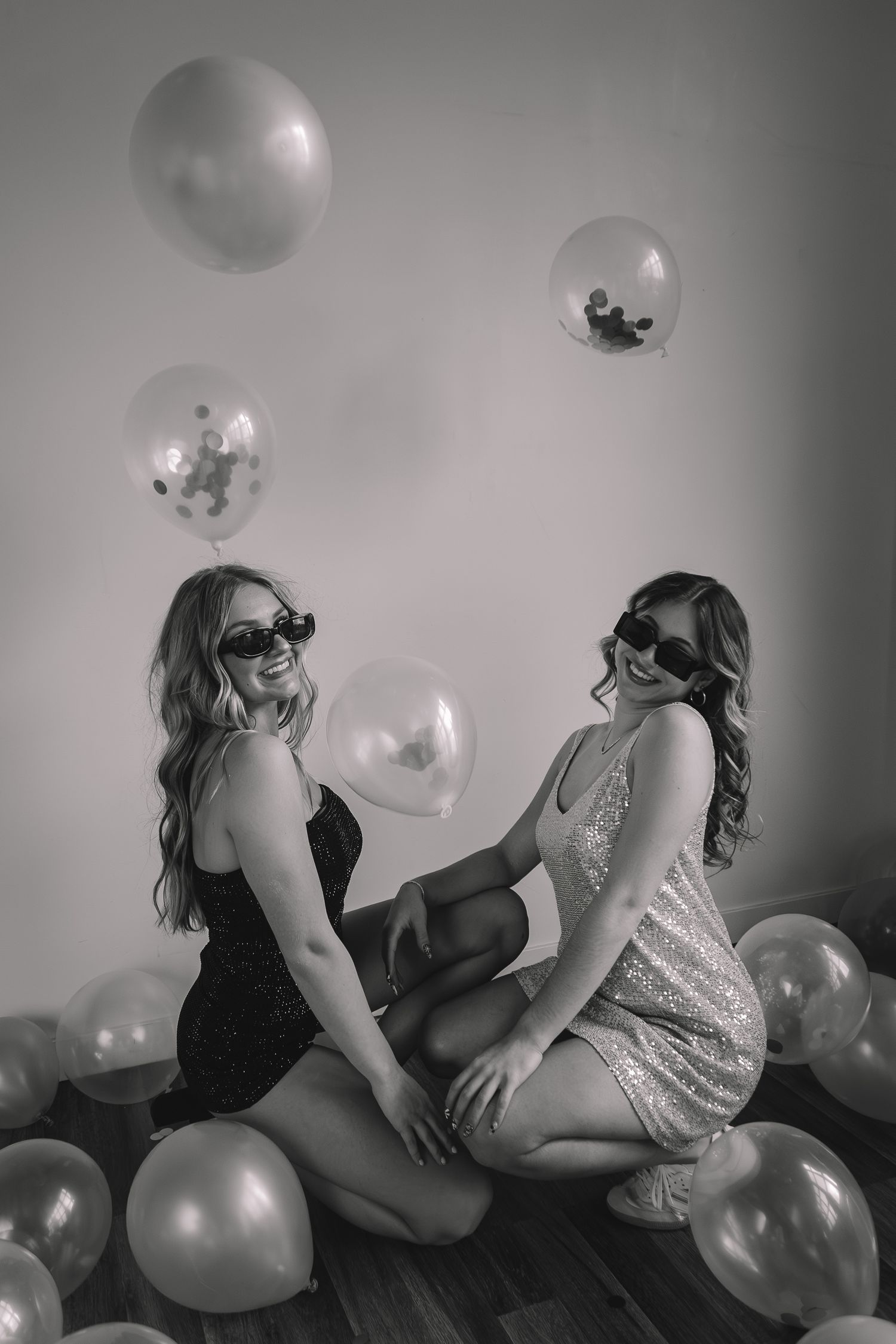 Monochrome photo of two people in contrasting outfits posing with balloons.