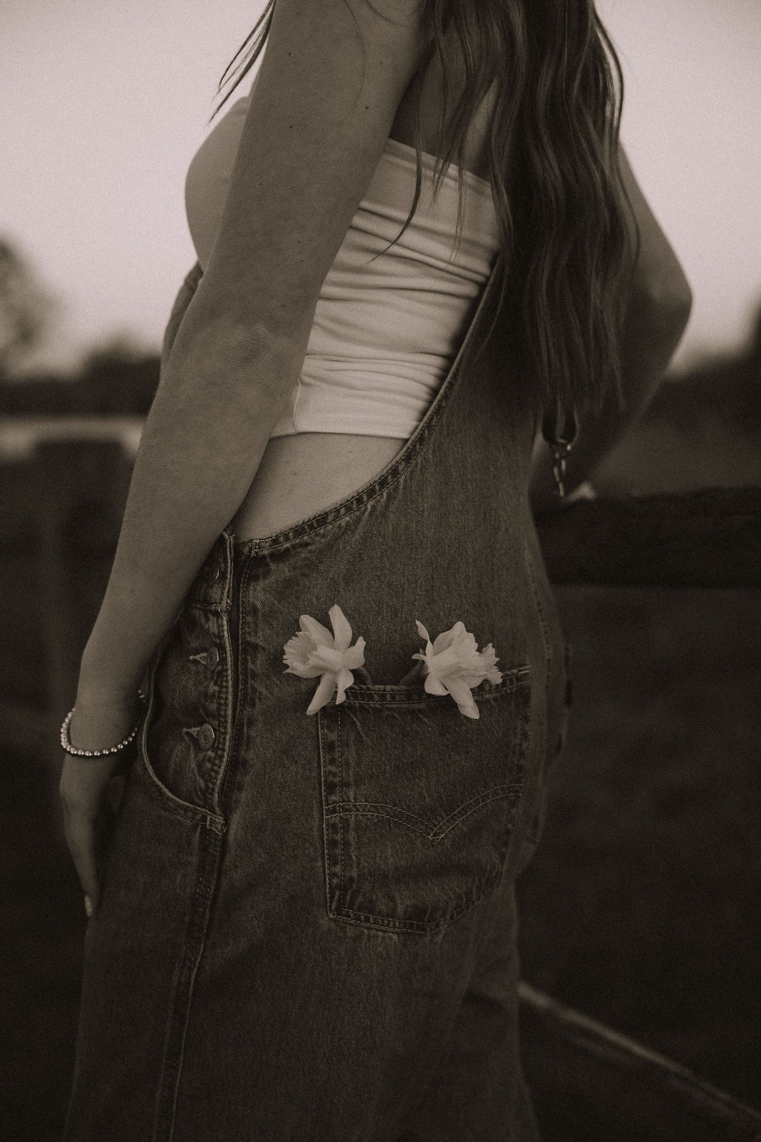 Black and white close-up of a woman in denim overalls with white flowers tucked into her pocket.