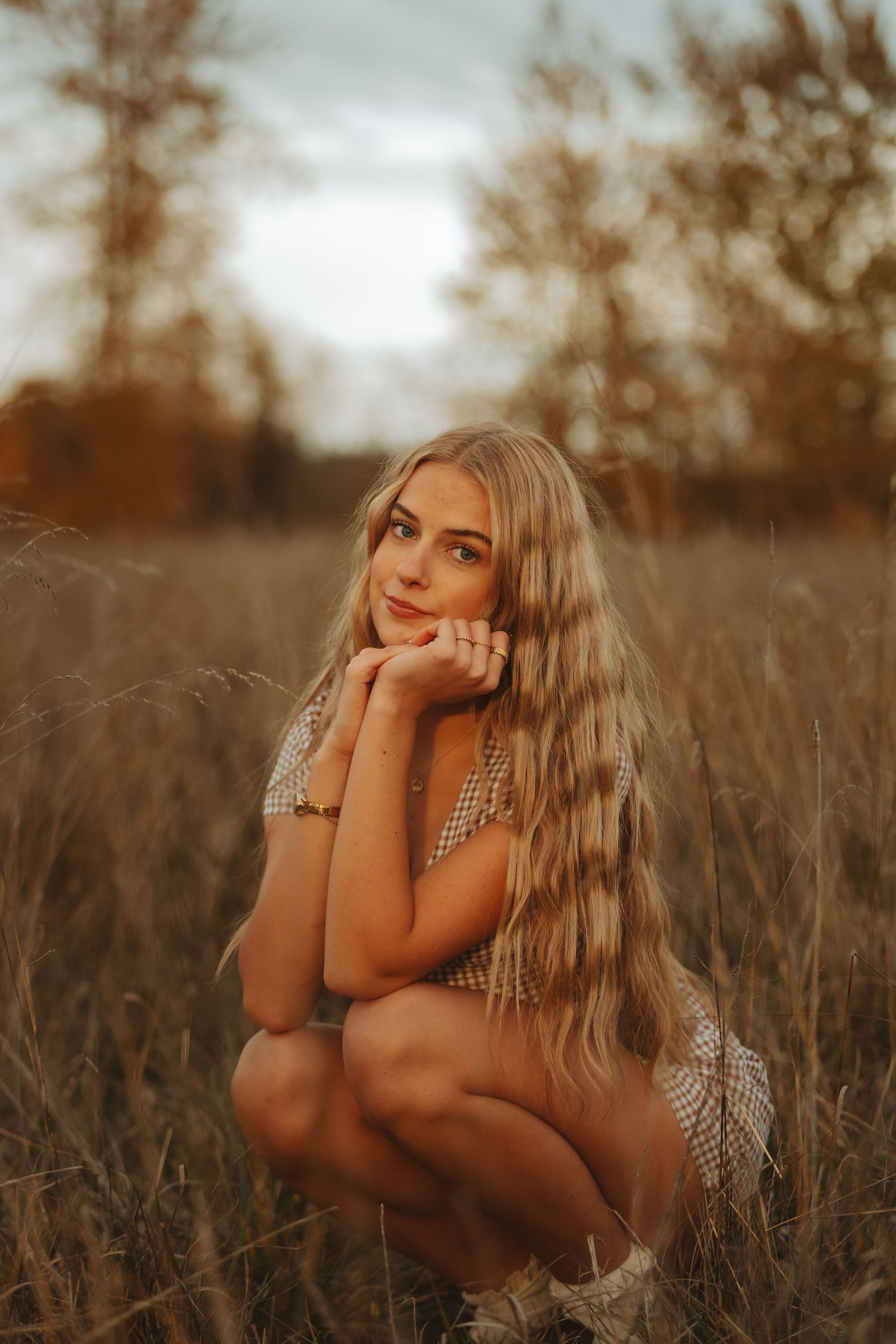 Person in plaid dress poses thoughtfully in tall grass during golden hour.