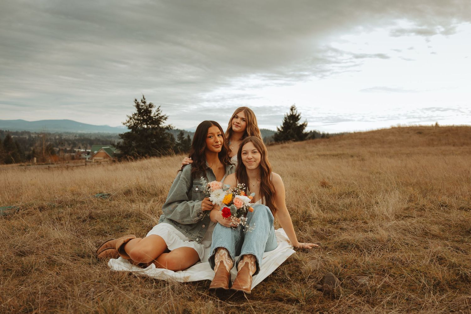 Friends wearing coordinated outfits relaxing in a rustic field with mountains visible in the distance.