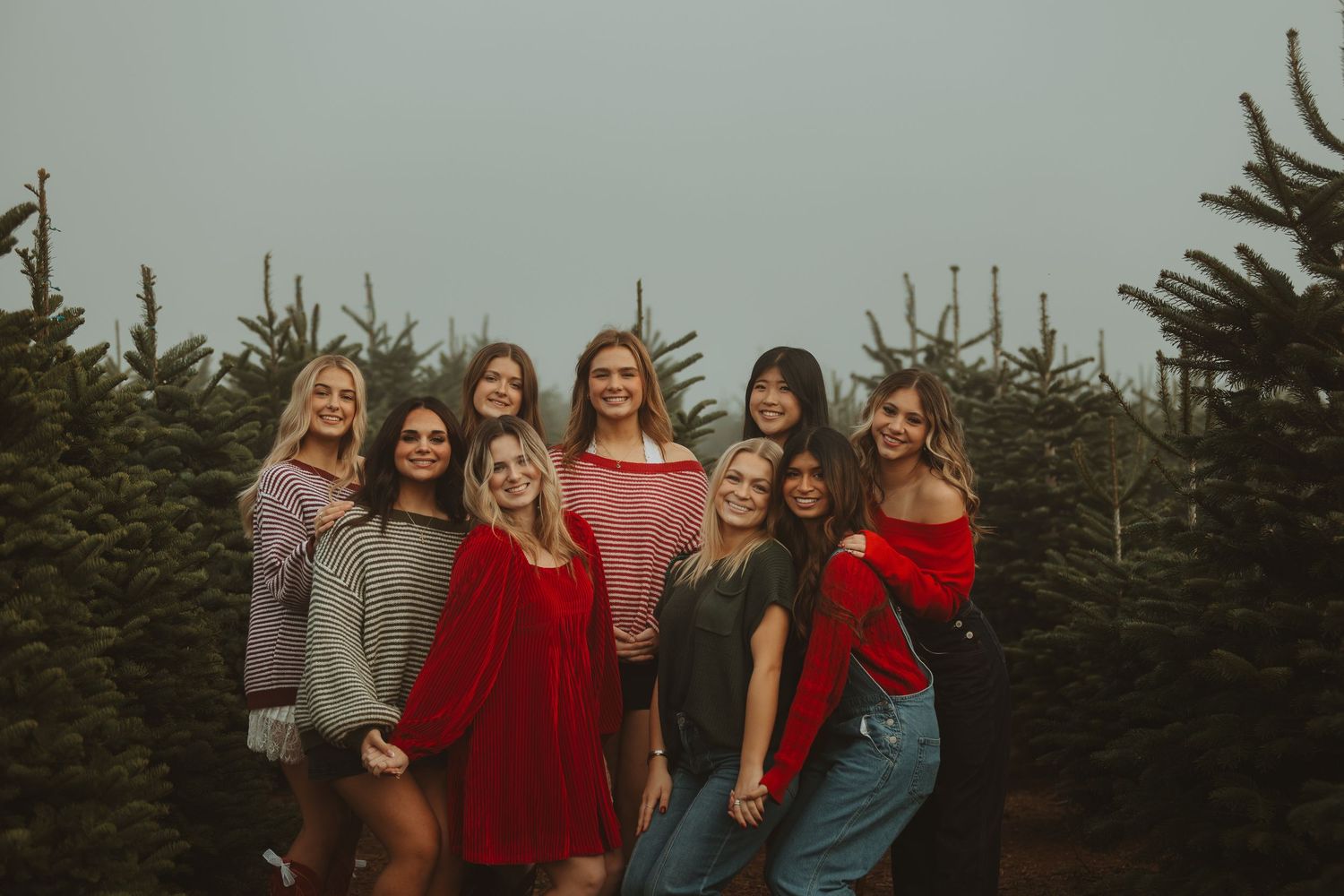 Friend group poses together among evergreen trees at dusk wearing casual fall outfits.