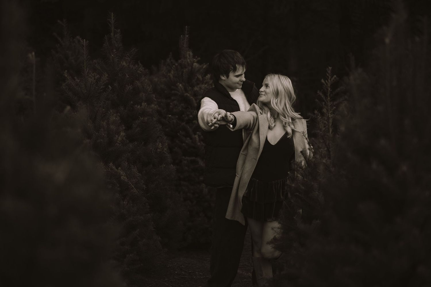 A moody black and white portrait of a person holding a vintage camera in a dark outdoor setting.