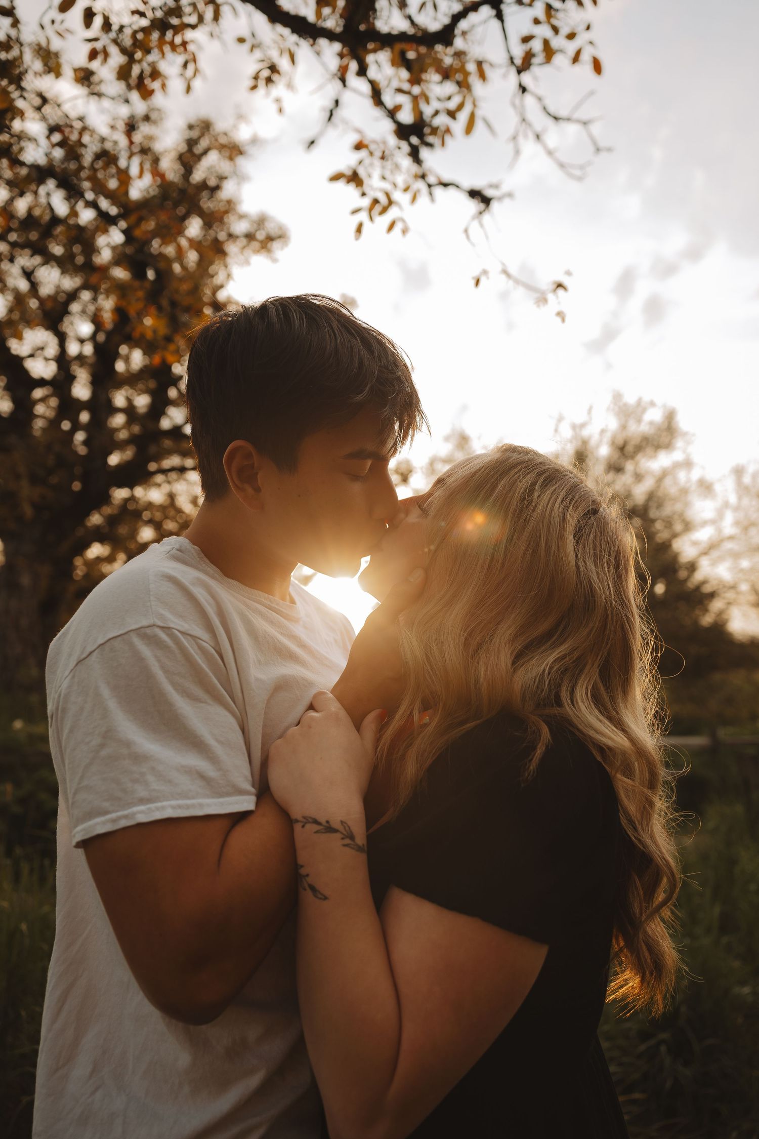 Couple sharing a romantic almost-kiss at sunset, backlit by warm golden light in a beautiful outdoor setting.