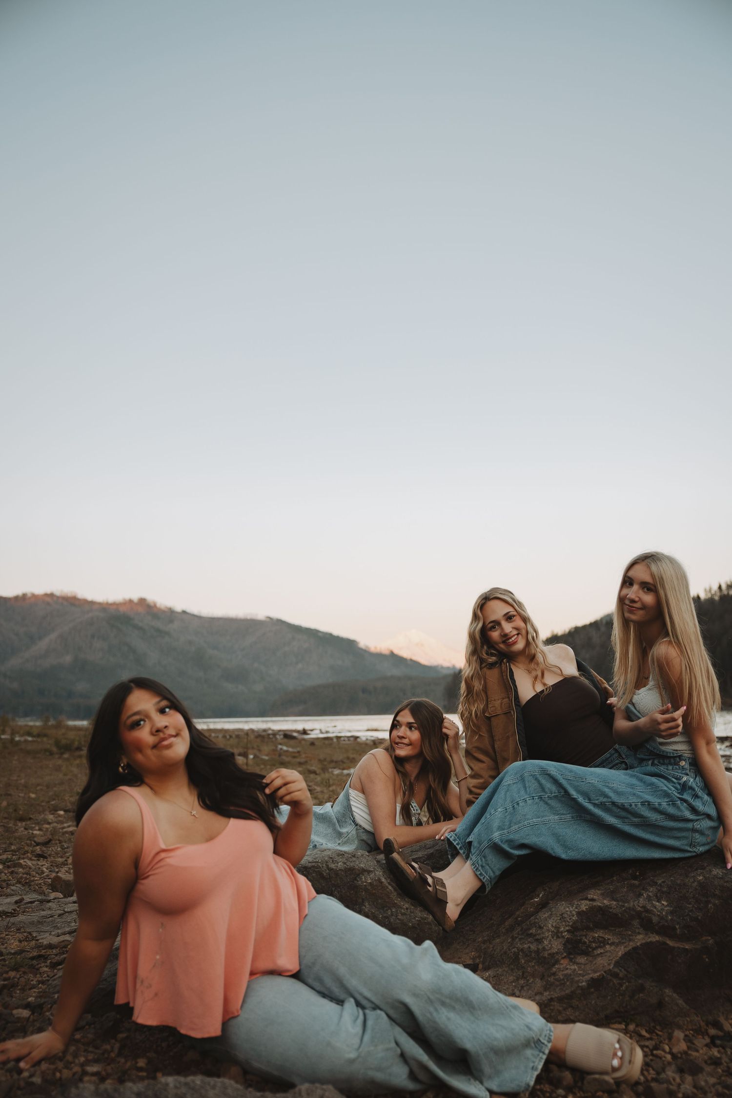 Four young women relaxing on rocks near a mountain lake during golden hour.