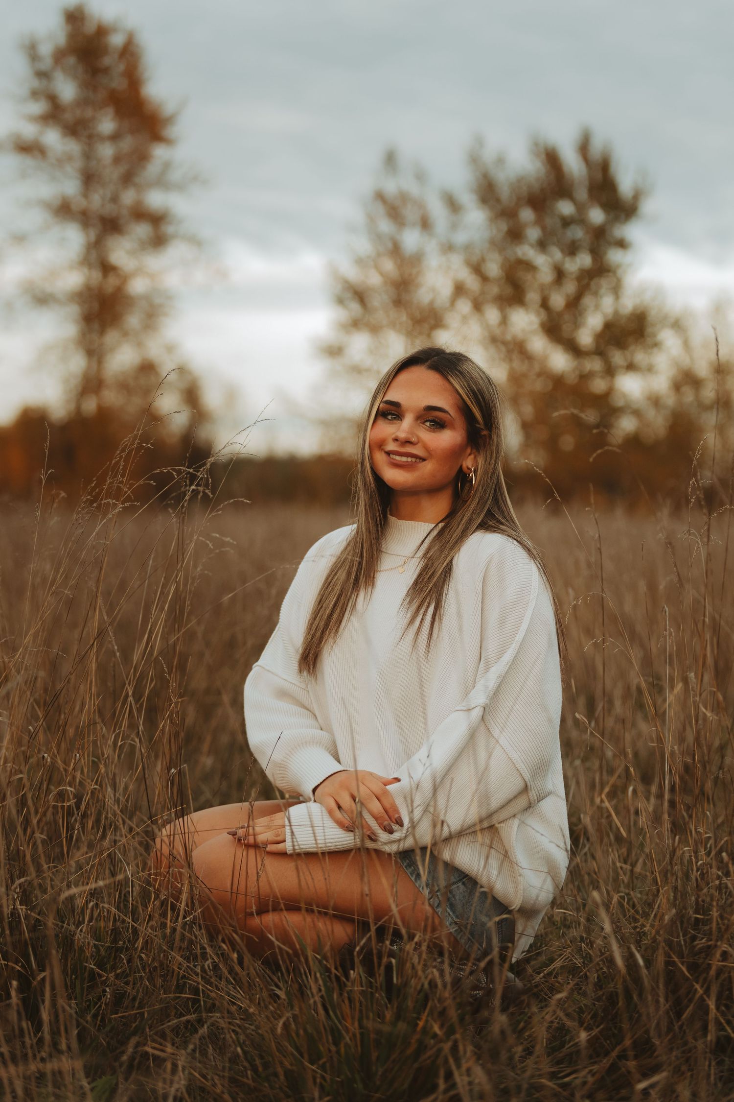 A person in white sits thoughtfully in a golden autumn field during sunset.