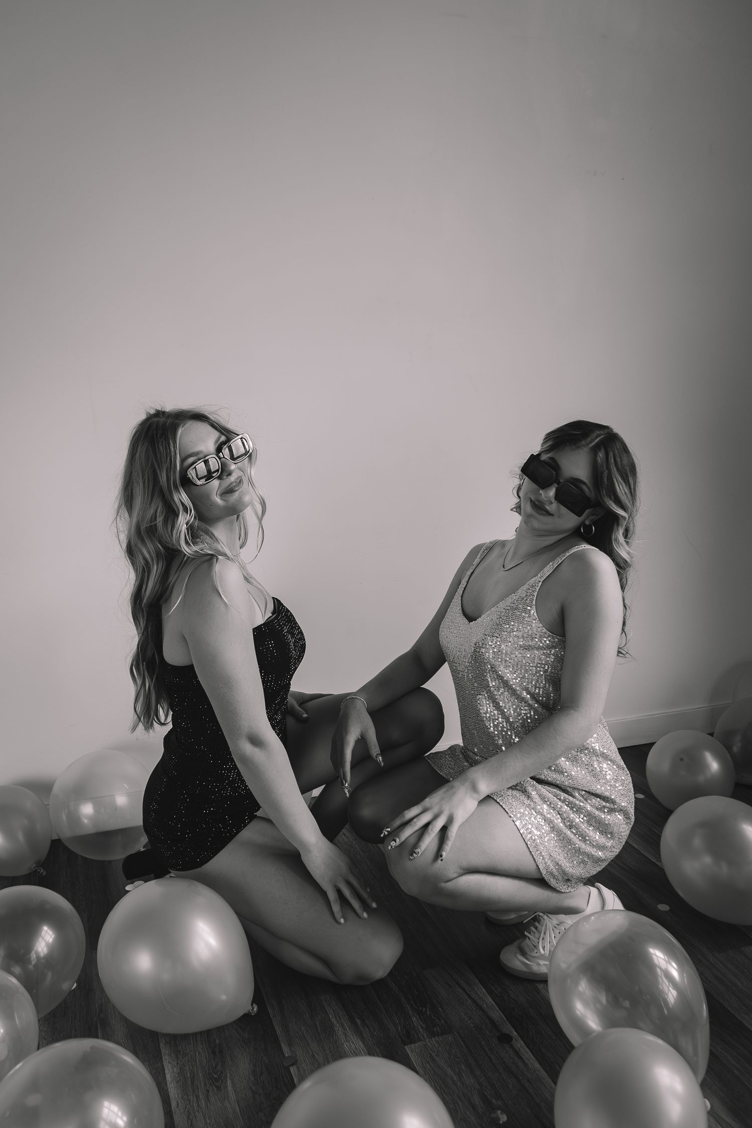 Artistic black and white portrait with two people and balloons on hardwood floor.