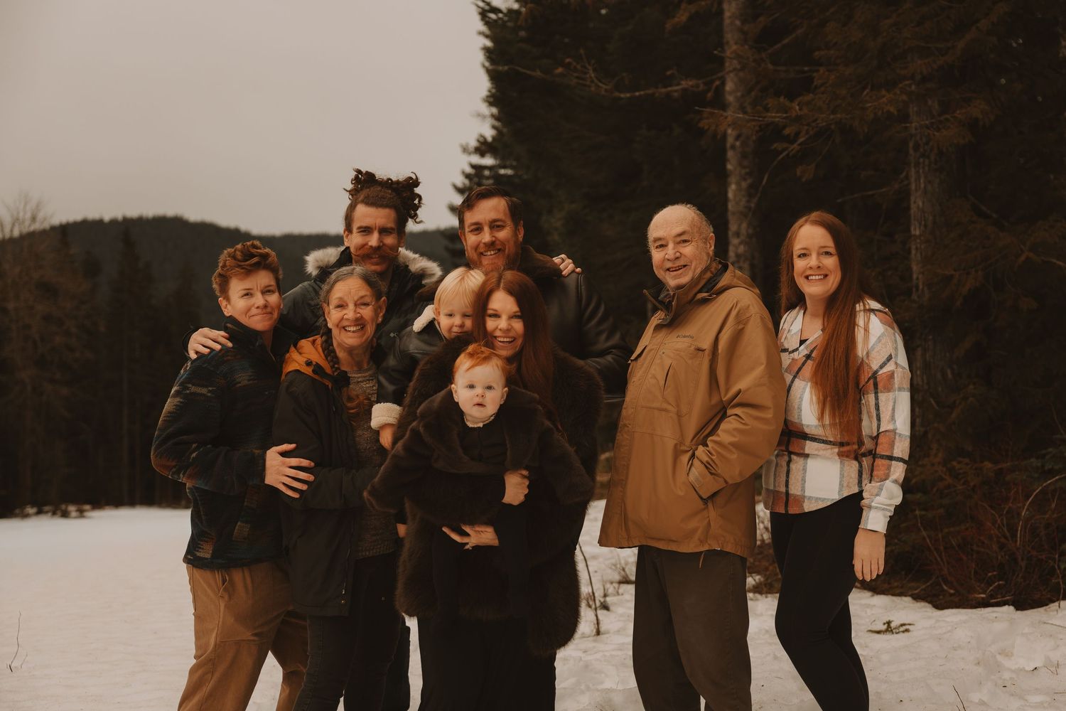 A group of people posing together outdoors in winter clothing against a snowy landscape background.