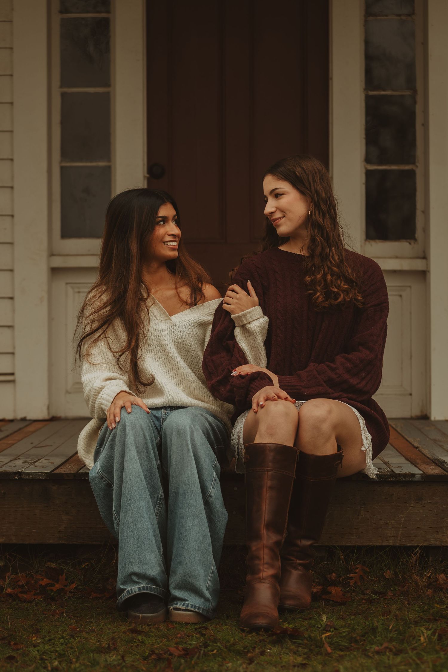 Two friends in casual attire sharing a conversation while sitting on wooden porch steps on an autumn day.