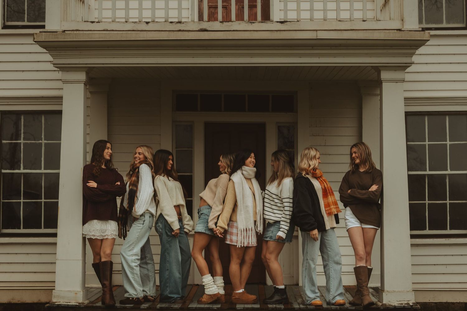 People in casual clothing stand in a line against a white building exterior with windows and architectural details.