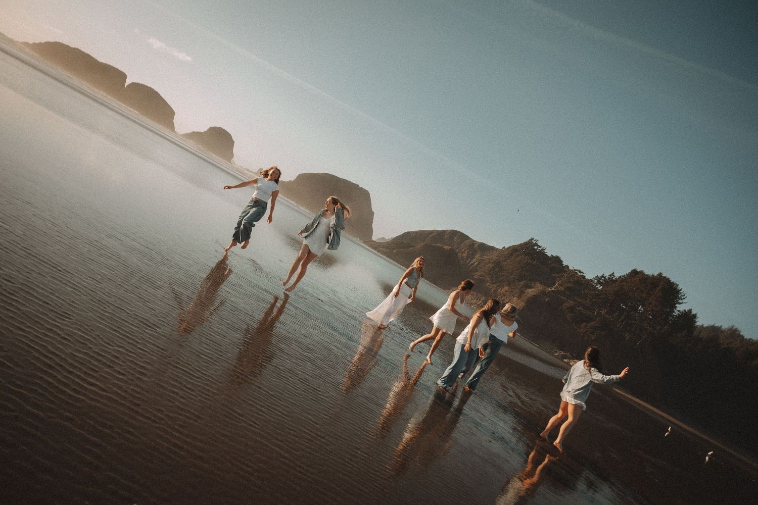 Women in flowing dresses spinning and dancing on a wet sandy beach during golden hour.
