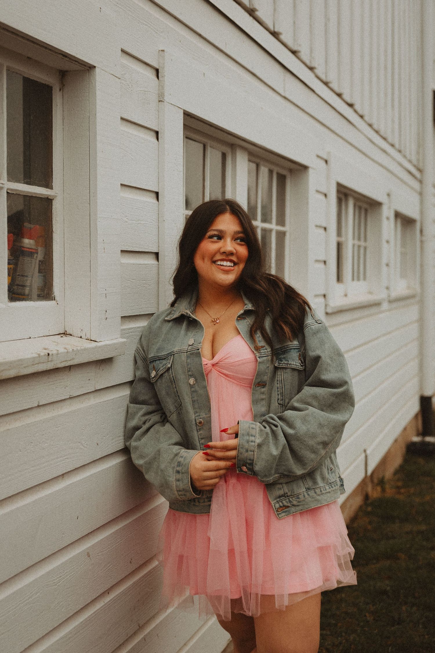 A fashion photoshoot against a white building featuring a pink tulle dress and denim jacket combination.