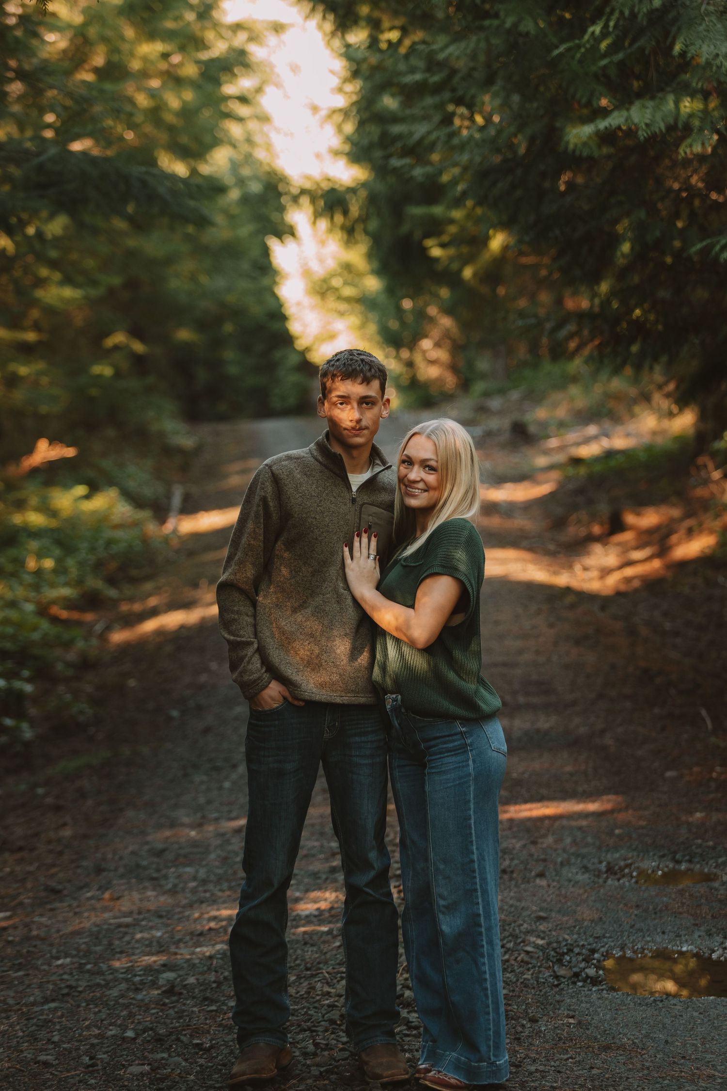 A couple shares an intimate moment while walking along a forested trail at sunset.