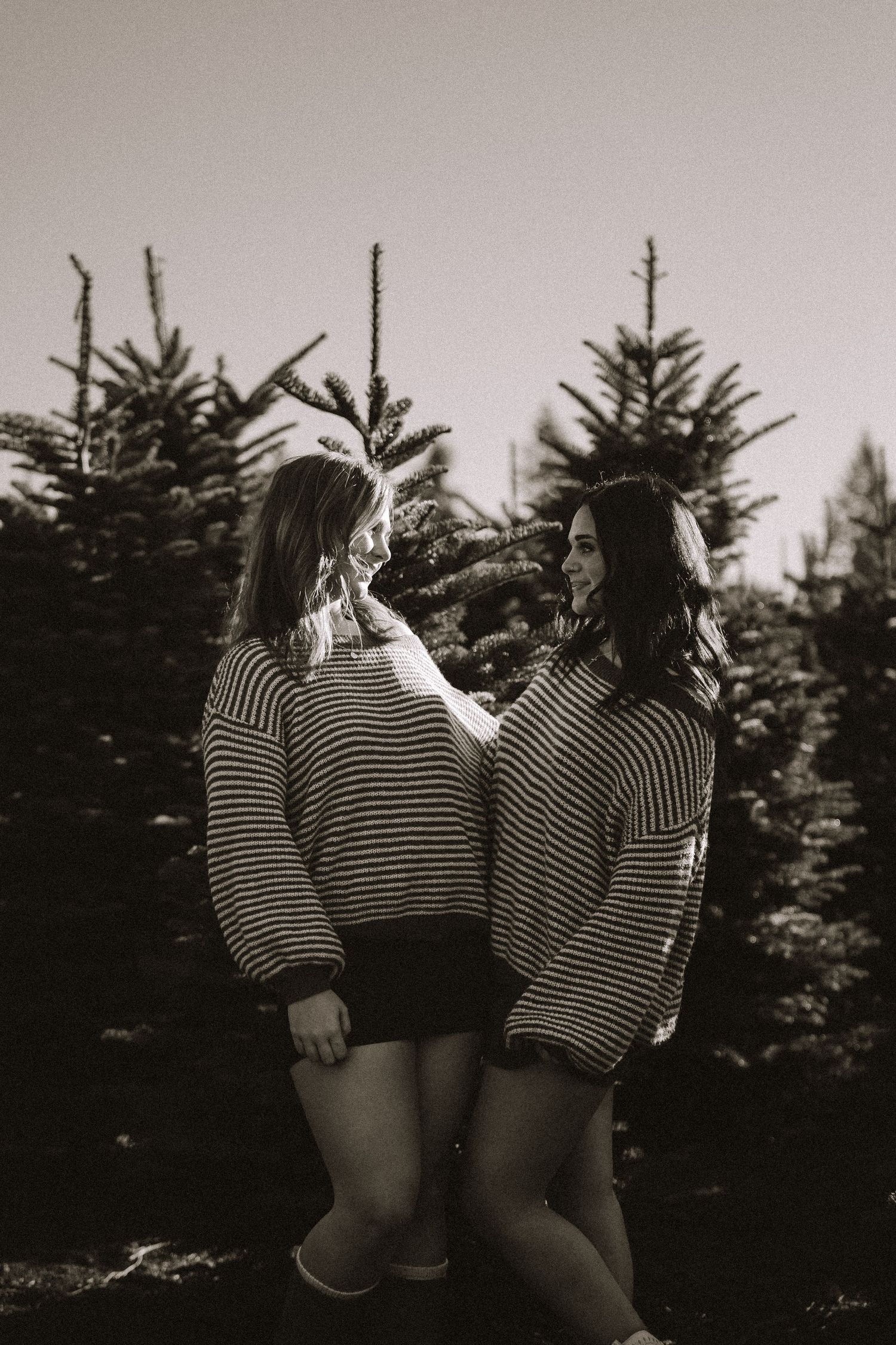 Black and white photo of people wearing matching striped shirts posing together near pine trees.