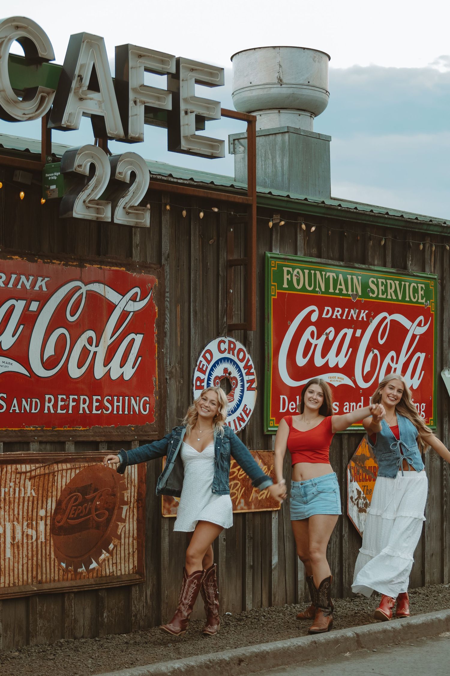 Vintage cafe and Coca-Cola signage displayed on rustic wooden wall under cloudy sky.