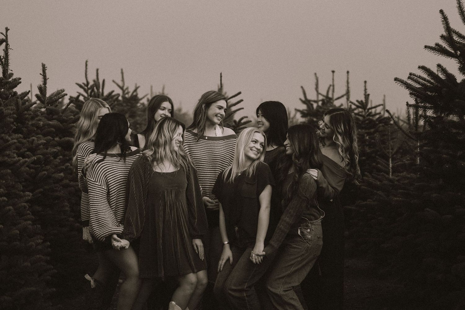 Black and white photo of group laughing together among pine trees.