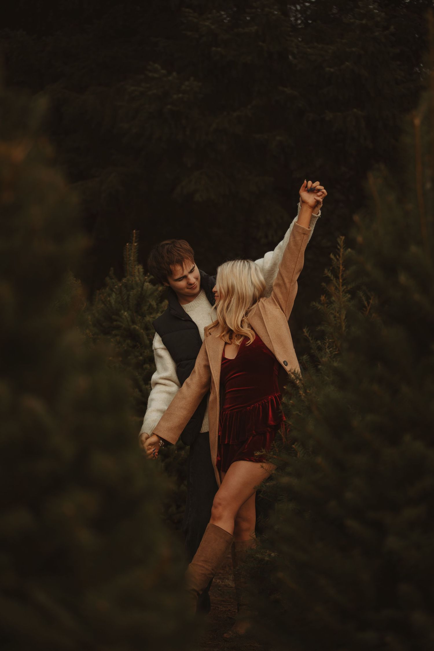 Dancing couple in autumn clothes share a romantic moment among evergreen trees.