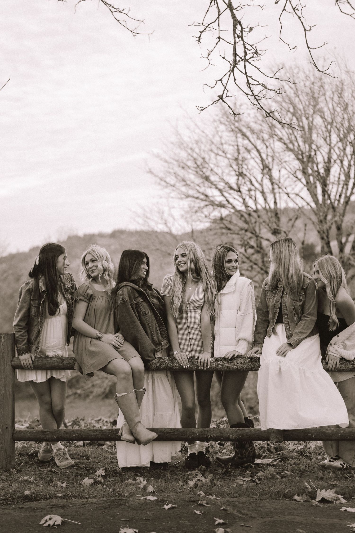 Vintage black and white photo of people sitting on a fence in rustic clothing.