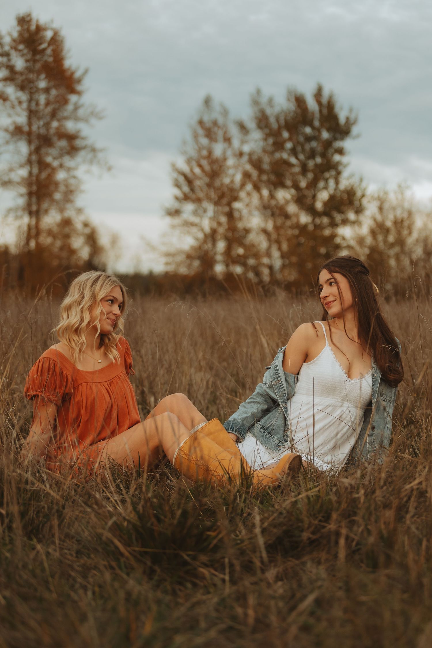 Friends in autumn-toned outfits lounge together in tall grass during sunset.