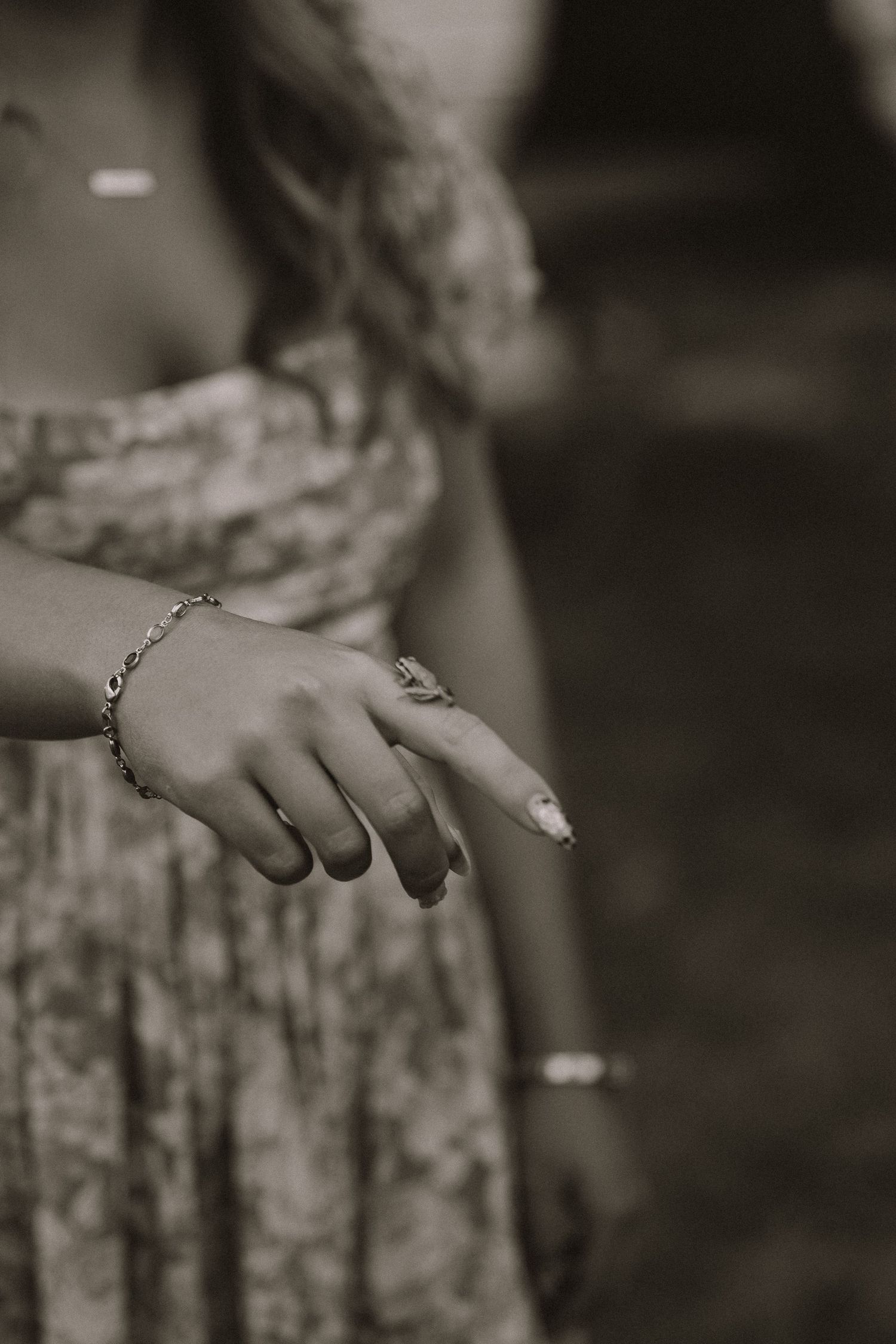 Black and white close-up of a woman's hand adorned with a bracelet and ring, wearing a floral dress.