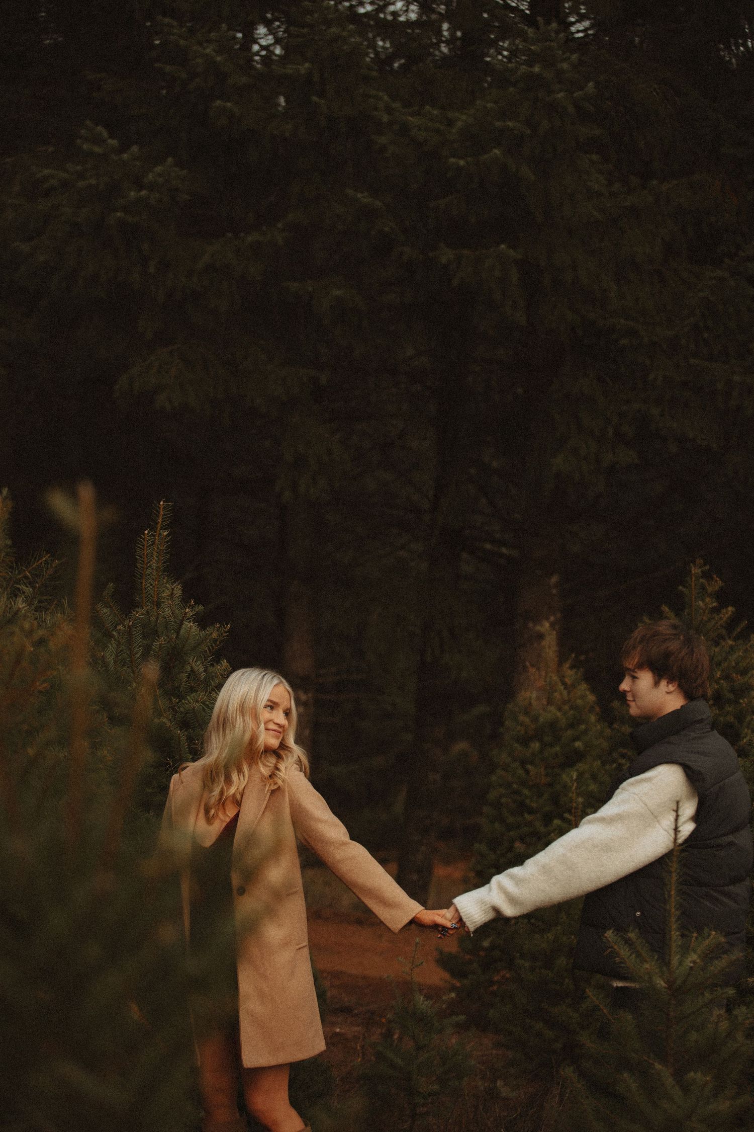Playful couple holding hands while walking through an evergreen forest.